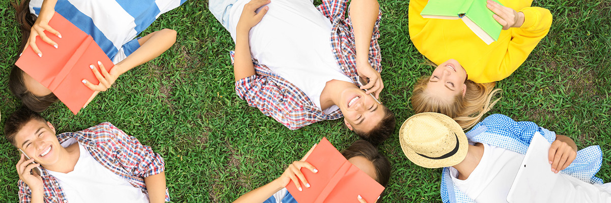 young men and women laying on the grass, reading and using the smartphone